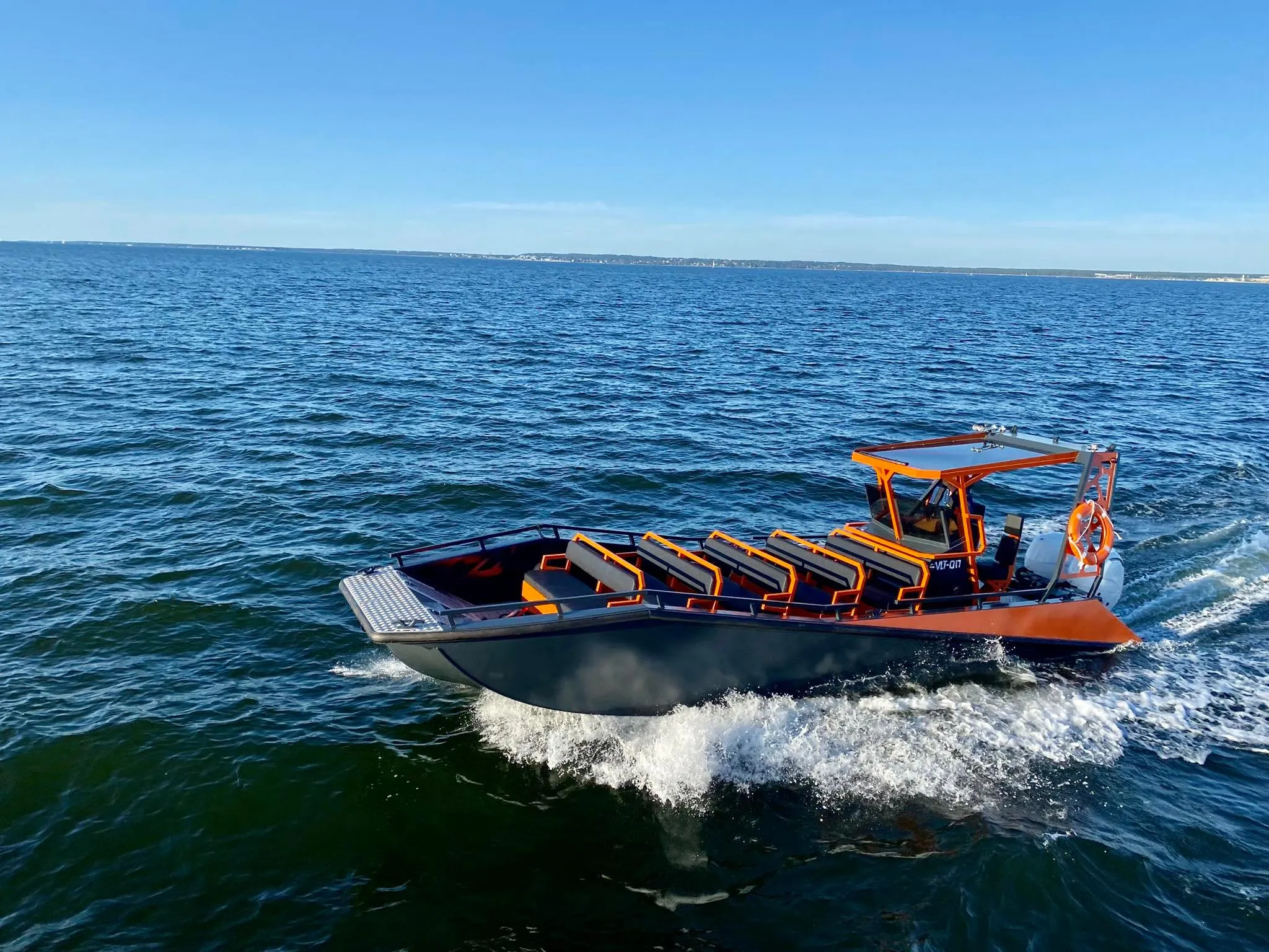 An LR9 Safari finished in orange underway on open water, its five empty passenger benches and centre walkway visible from the bow quarter