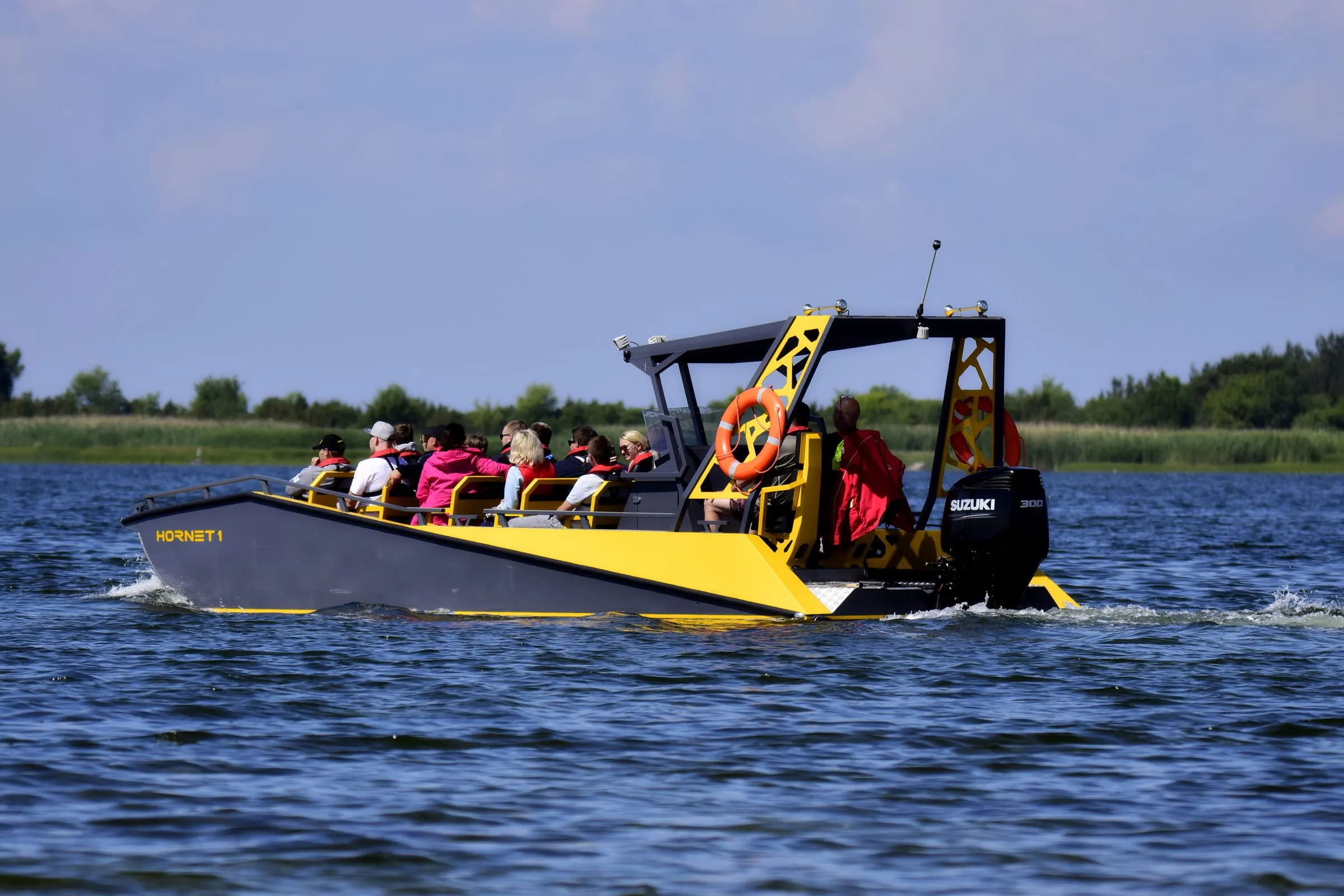 An LR9 Safari underway on open water with a full load of passengers seated on the forward benches and two crew at the helm behind them